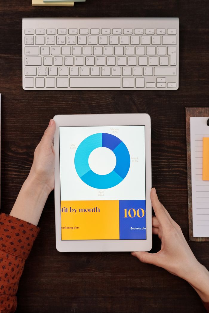our-story A person holds a tablet showing a business graph next to a keyboard on a wooden desk.