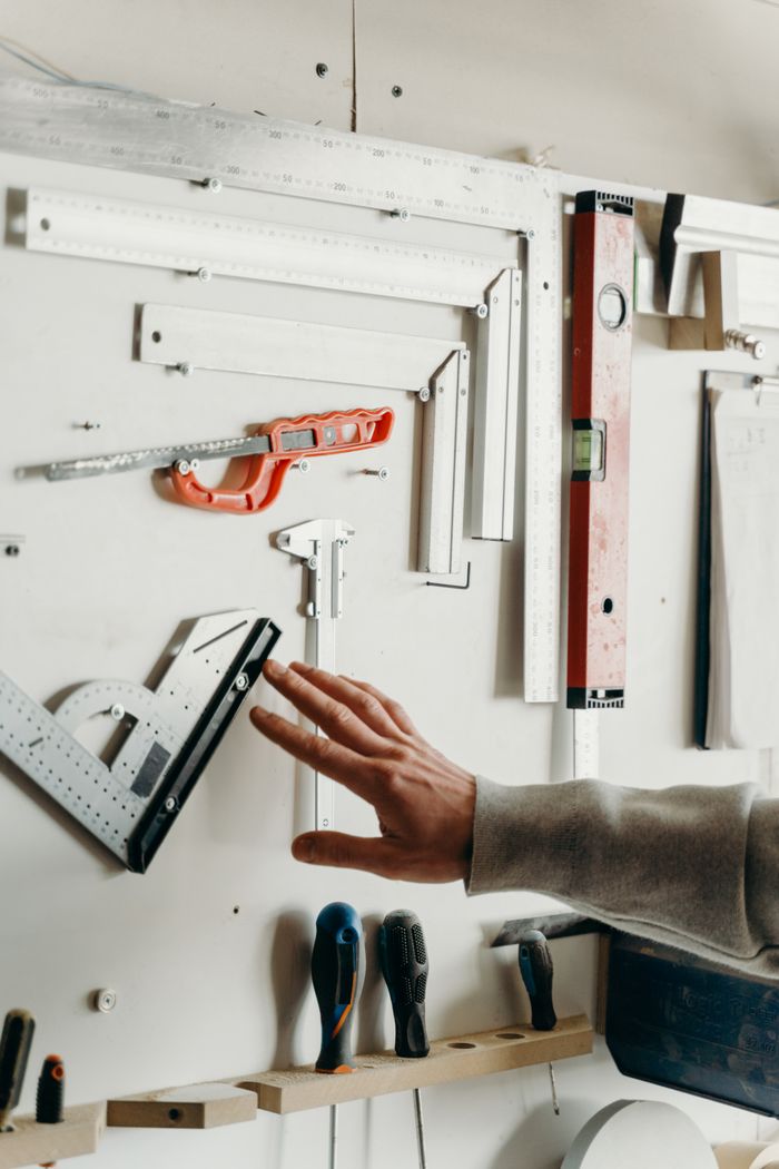 Hand selecting tool from well-organized carpentry wall display. Ideal for woodworking content.