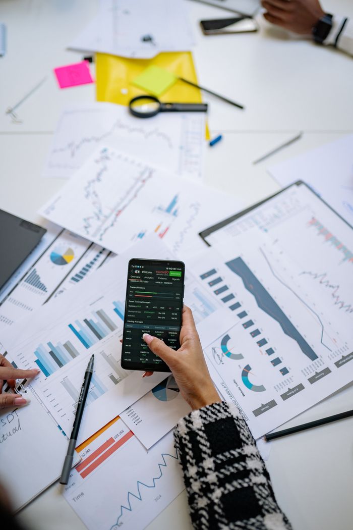 who-we-are Person analyzes financial charts using a smartphone in an office setting.